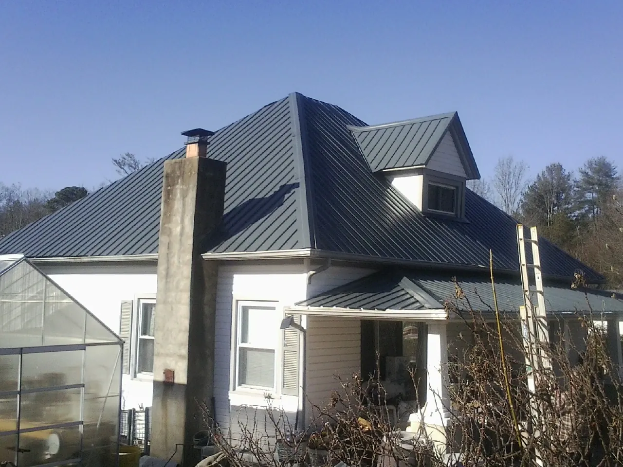 Dark blue standing seam metal roof on a white farmhouse with dormer — Slate & Tile Roof Repair by Roofing Brothers in Antigo