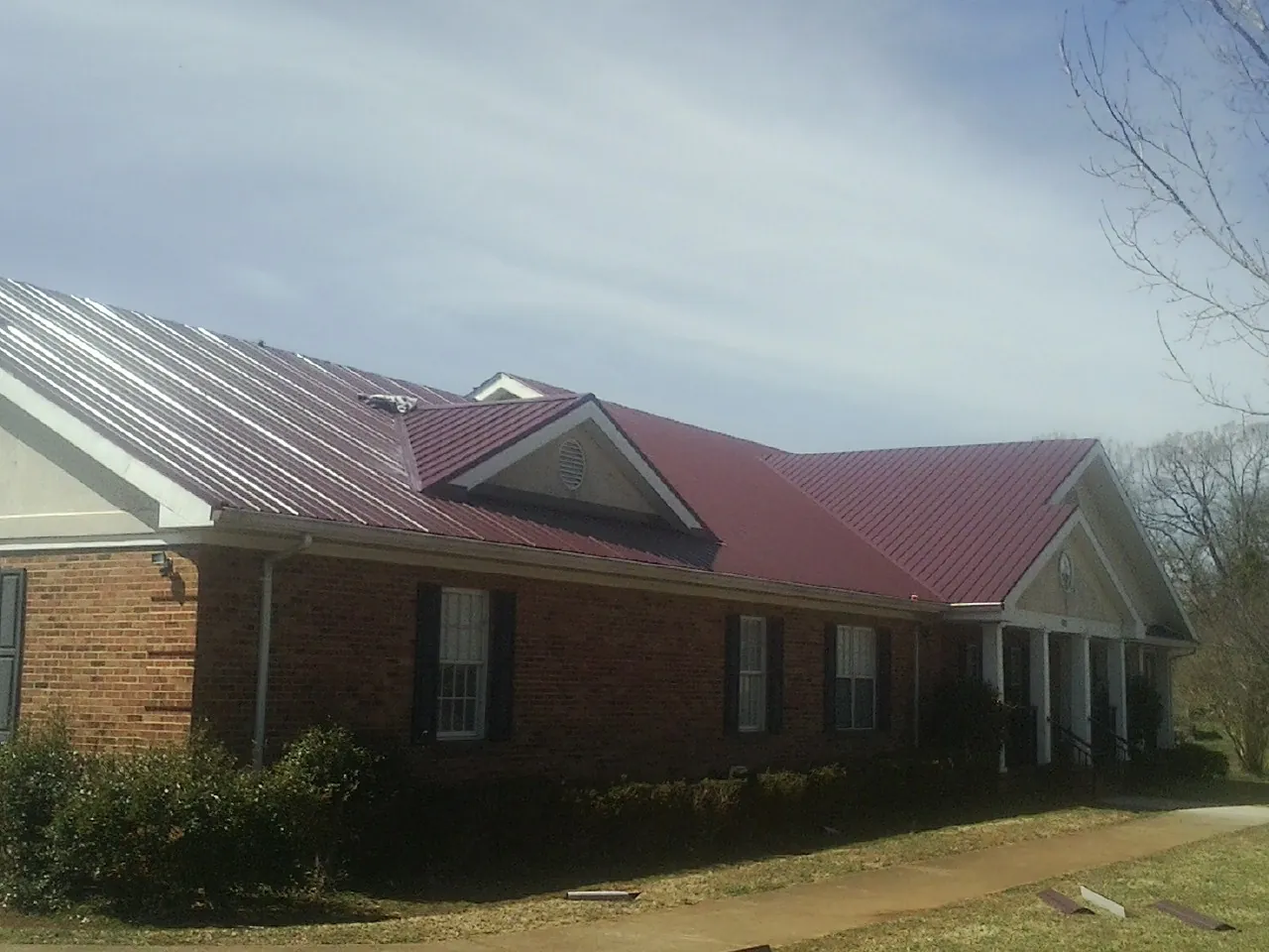 Red metal roof with gabled entries on a long brick building, from a Hail Damage Roof Repair job in Antigo