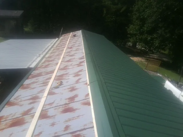 Old rusted panels beside newly installed green metal roofing — Wind Damage Roof Repair by Roofing Brothers in Antigo