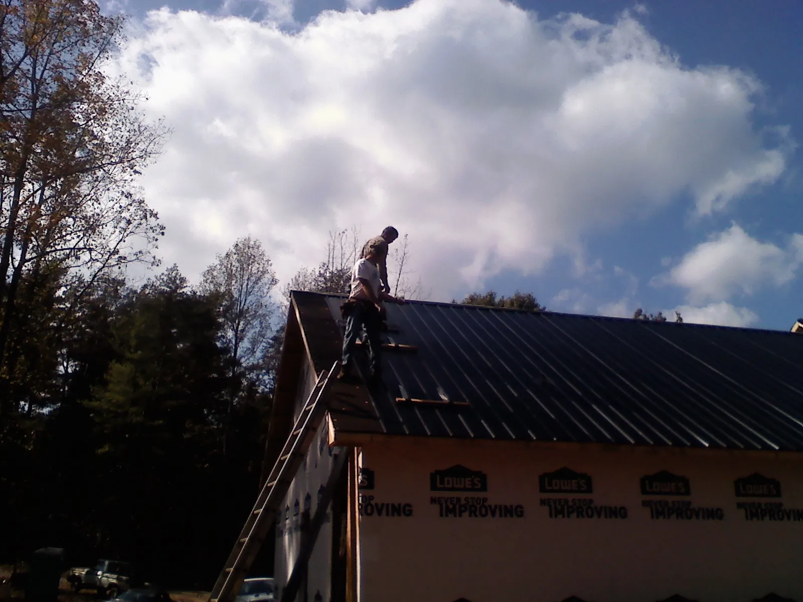 Roofer fastening dark metal panels high against a cloudy sky, from a Roof Inspection job in Antigo
